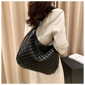 Detail of the glossy quilted texture and wide strap on the large black hobo shoulder bag
