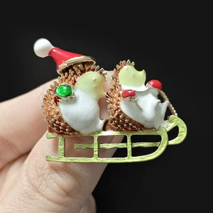 Detailed close-up of a Christmas hedgehog brooch with red hat and gold sleigh base