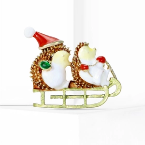 Detailed view of two cute hedgehogs with a red Santa hat on a golden sleigh brooch