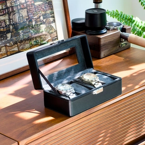 Detail of a 2-slot black leather watch box with glass window and metal lock on a wooden desk
