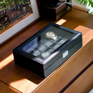 Detail of 12-slot black leather watch box with glass lid on a premium wooden desk