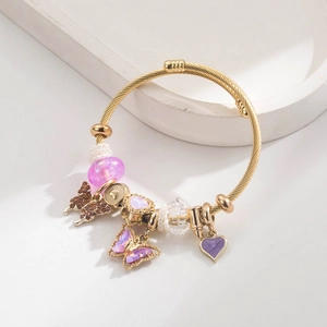 Detailed macro view of golden twisted bangle featuring butterfly and heart-shaped pendants