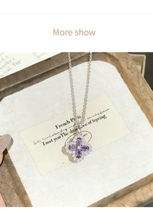 Detailed close-up of a silver four-leaf clover necklace with purple stones on white linen