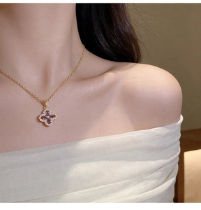 Close-up of golden four-leaf clover pendant with purple stones and white crystals