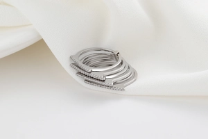 Macro detail of multi-layered silver rings with geometric zircons on white silk fabric