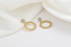 Détail de boucles d'oreilles cercles dorés avec micro-cristaux sur fond de satin blanc chic