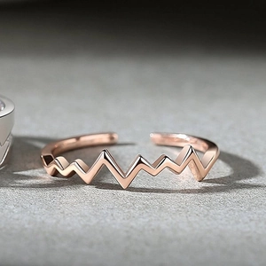 Macro shot of rose gold heartbeat ring with adjustable open design on gray surface