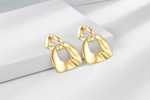 Close-up of gold irregular geometric drop earrings with a polished mirror finish on white