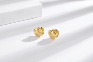 Macro shot of 18k gold shell earrings with detailed radial stripes and artistic shadows