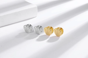 Detailed close-up of gold and silver shell-shaped hoop earrings with vertical stripe texture