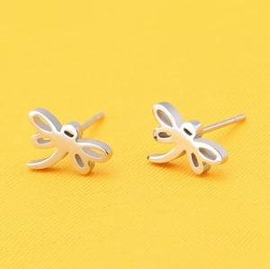 Close-up of silver dragonfly stud earrings showing intricate wing texture on yellow fabric