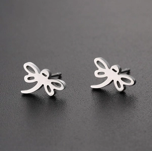 Minimalist silver dragonfly stud earrings with hollow wings on dark textured surface