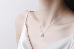 Close-up of a silver necklace with a round light blue gemstone on a female model