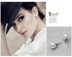 Detailed view of round white pearl earrings with silver needles on a model and close-up