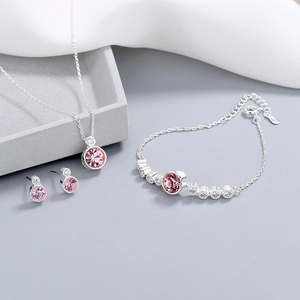 Pink crystal jewelry set with silver necklace bracelet and earrings on a tray