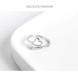 Detail of silver heart-shaped open ring with a round zircon on white platform