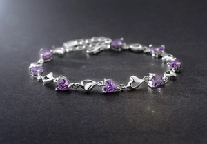 Détail d'un bracelet cœur argenté avec cristaux violets et chaîne réglable sur pierre