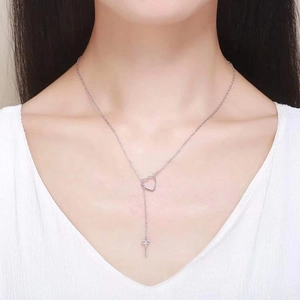 Detail view of silver heart and key pendant necklace worn on neck by a model