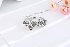 Detail of bee and daisy ring with yellow gemstones and white zircons on a white card