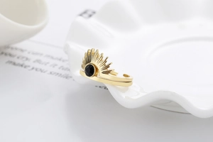 Detail of adjustable gold sunflower ring with black gemstone on white ceramic plate