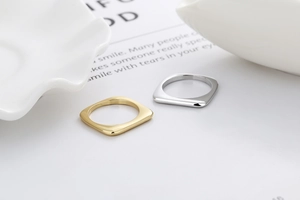 Polierte quadratische Ringe in Gold und Silber auf einem weißen strukturierten Tablett