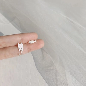 Detail of silver asymmetric earrings featuring cute cat and fish shapes on hands