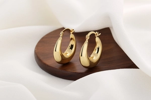 Detailed close-up of 18K gold plated hollow crescent hoop earrings on a wooden plate