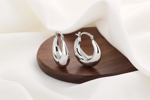 Macro shot of silver teardrop hoop earrings on a dark wood base with white silk