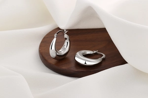 Detailed close-up of chunky silver teardrop hoop earrings on a wooden tray display