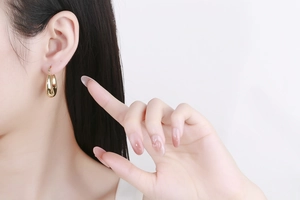 Detail of 18K gold hollow crescent hoop earring shown on model with shiny metallic finish