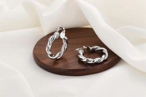 Détail des boucles d'oreilles créoles torsadées argentées sur bois et soie blanche