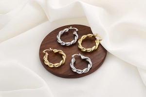 Détails de boucles d'oreilles créoles torsadées or et argent sur bois et soie blanche