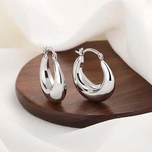 Polished silver hollow teardrop hoop earrings on a wooden stand with silk fabric