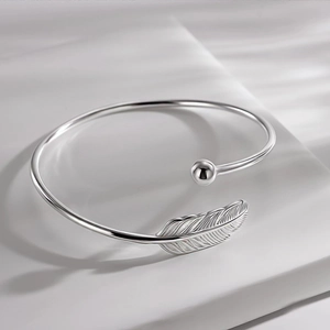 Elegant silver feather open cuff bracelet with minimalist polished bead on white fabric