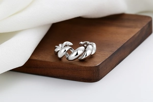 Close-up of twisted silver-colored open ring on a dark wooden display stand
