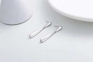 Detailed view of long polished silver teardrop earrings with a mirror finish on white background