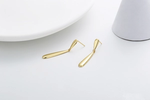 Detailed view of long tapered gold drop earrings with a polished mirror finish on white props