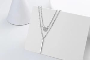 Detail of layered silver necklace featuring a sparkling round pendant and vertical bar