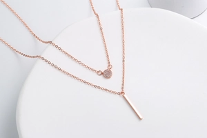 Detail of rose gold double layer necklace with a round zircon and vertical bar pendant