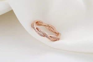 Détail de la bague entrelacée en or rose avec cristaux pavés sur tissu blanc