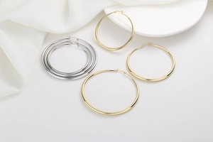 Detailed view of polished gold and silver hoop earrings in multiple sizes on white fabric