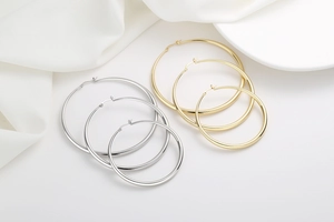 Close-up of polished gold and silver hoop earrings in three sizes on white silk