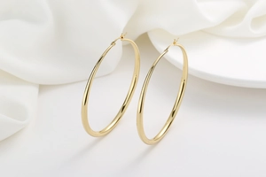 Close-up of polished gold large hoop earrings on elegant white silk background