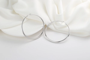 Close-up of large polished silver hoop earrings on elegant silk background
