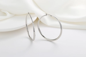 Close-up of polished silver hoop earrings with S925 hallmark on minimalist silk background