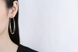 Close-up of a large silver polished hollow hoop earring worn by a female model