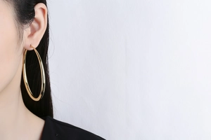 Detail of a large polished gold hoop earring worn on a model with glossy finish