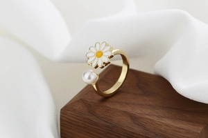 Detail of adjustable gold ring with daisy flower and pearl on wooden background