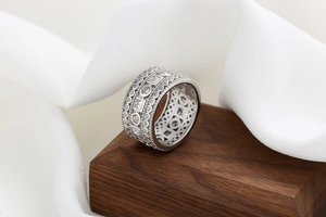 Macro shot of silver-colored hollow wide band ring with cubic zirconia on walnut wood