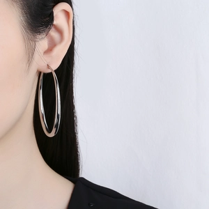 Minimalist large silver hoop earrings featuring a hollow geometric design on female model